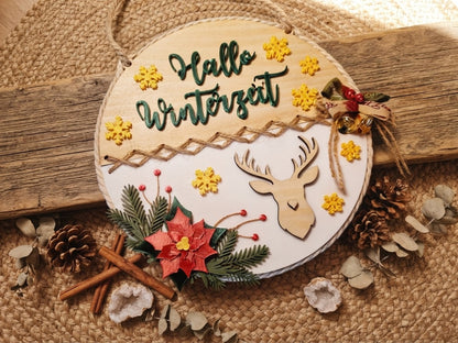 Nahaufnahme des runden Hallo Winterzeit Schilds mit gelben Schneeflocken und Hirschmotiv